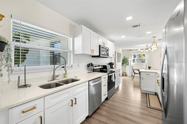 kitchen with pendant lighting, sink, hardwood / wood-style floors, stainless steel appliances, and white cabinets