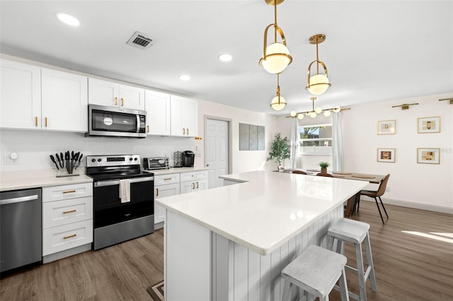 kitchen with a kitchen island, pendant lighting, white cabinets, a kitchen breakfast bar, and stainless steel appliances