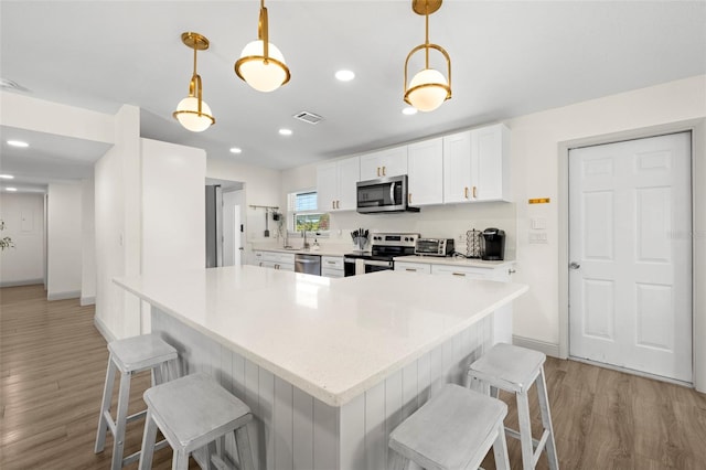 kitchen featuring appliances with stainless steel finishes, a kitchen breakfast bar, decorative light fixtures, and white cabinets