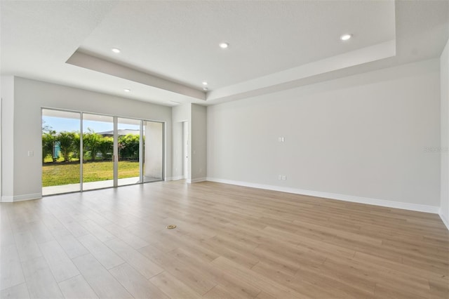 spare room with a raised ceiling and light wood-type flooring