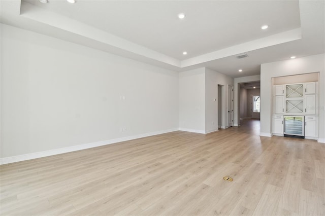 spare room featuring wine cooler, indoor bar, a raised ceiling, and light wood-type flooring