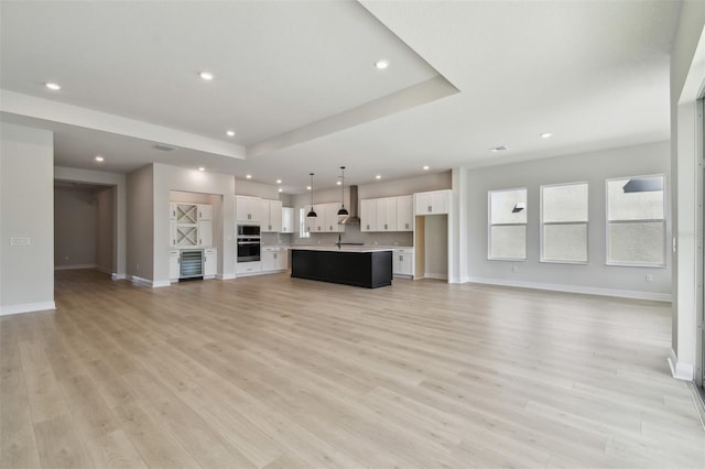 unfurnished living room with wine cooler, sink, a tray ceiling, and light hardwood / wood-style flooring