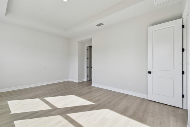 empty room featuring a tray ceiling and light wood-type flooring