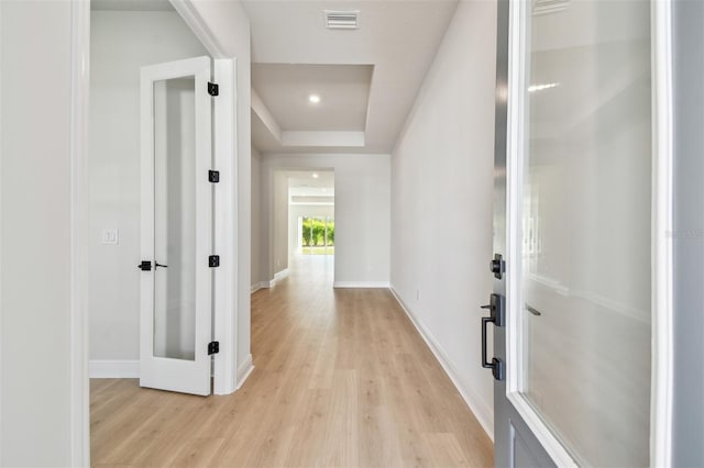 hallway featuring light wood-type flooring and a tray ceiling