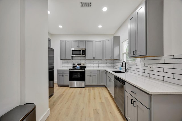 kitchen with sink, light stone counters, light wood-type flooring, gray cabinets, and stainless steel appliances