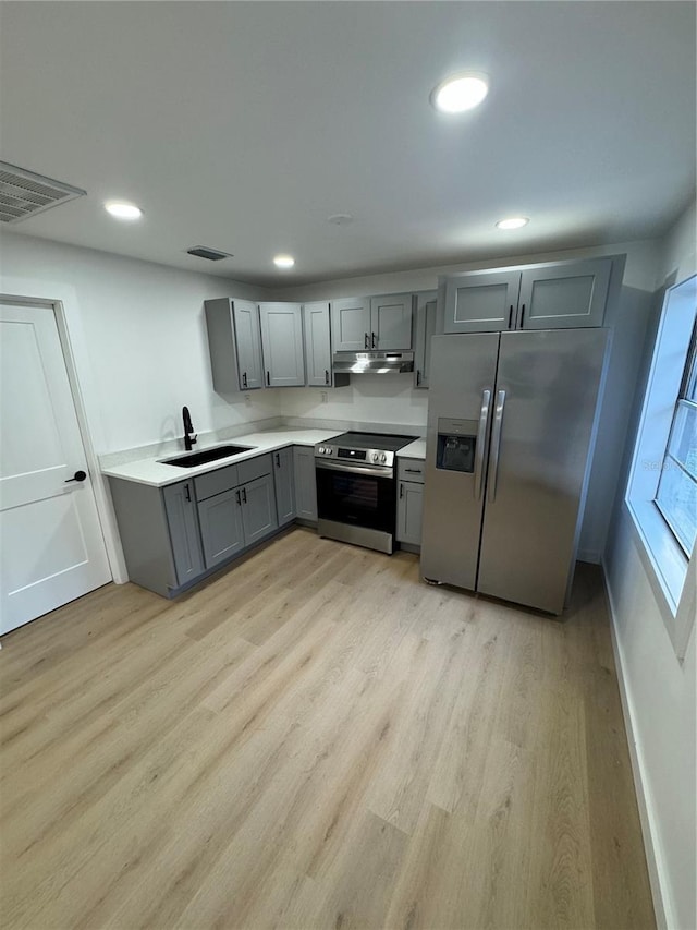 kitchen with appliances with stainless steel finishes, gray cabinets, sink, and light hardwood / wood-style flooring