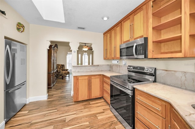 kitchen featuring ceiling fan, appliances with stainless steel finishes, a skylight, a textured ceiling, and light wood-type flooring