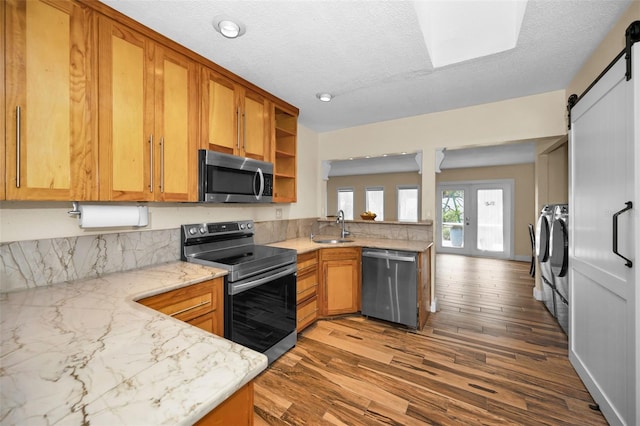 kitchen with appliances with stainless steel finishes, washer and dryer, sink, kitchen peninsula, and a barn door