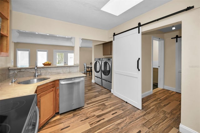 kitchen with sink, a skylight, independent washer and dryer, stainless steel dishwasher, and a barn door