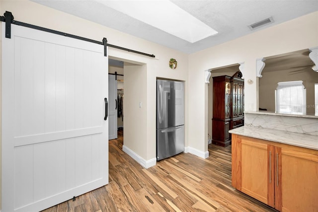 kitchen with stainless steel refrigerator, a barn door, light stone counters, and light wood-type flooring