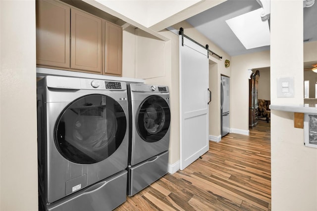 clothes washing area featuring light hardwood / wood-style flooring, a skylight, cabinets, separate washer and dryer, and a barn door