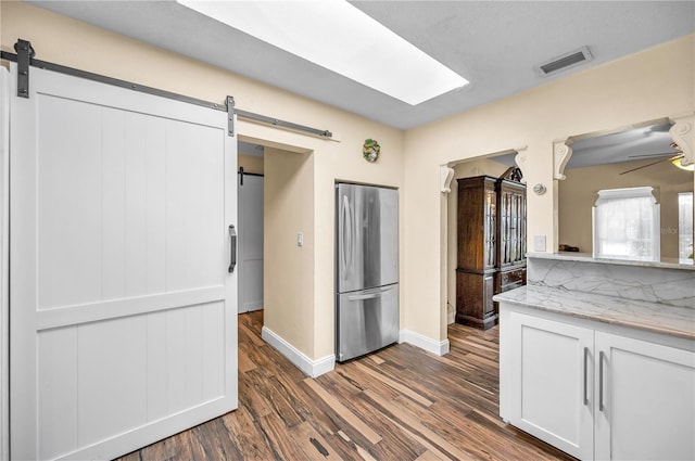 546 Orangewood Dr, Dunedin, FL 34698 - kitchen featuring freestanding refrigerator, a barn door, dark wood-style floors, baseboards, and white cabinets