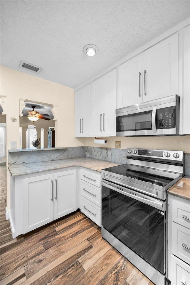 546 Orangewood Dr, Dunedin, FL 34698 - kitchen with appliances with stainless steel finishes, a ceiling fan, white cabinetry, wood finished floors, and a textured ceiling