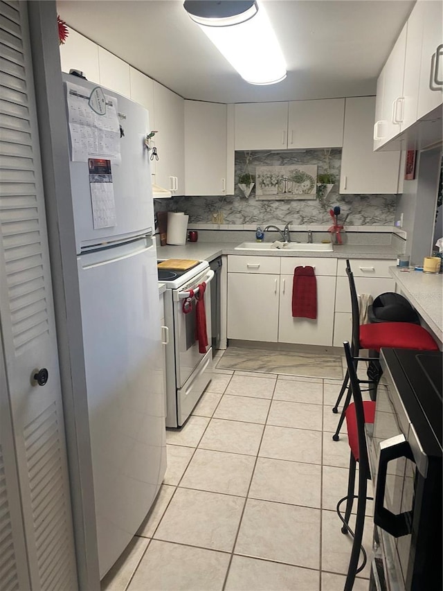 kitchen featuring light tile patterned flooring, sink, tasteful backsplash, white appliances, and white cabinets