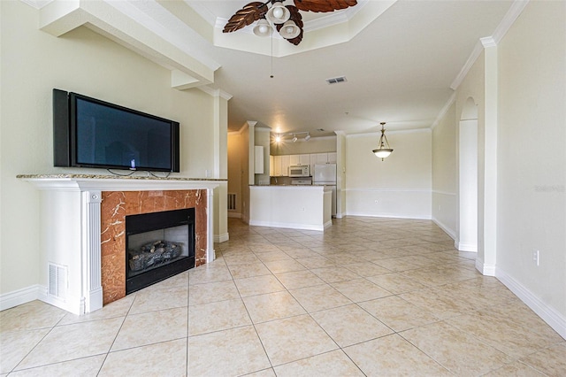 unfurnished living room with a tray ceiling, light tile patterned floors, a tile fireplace, and crown molding