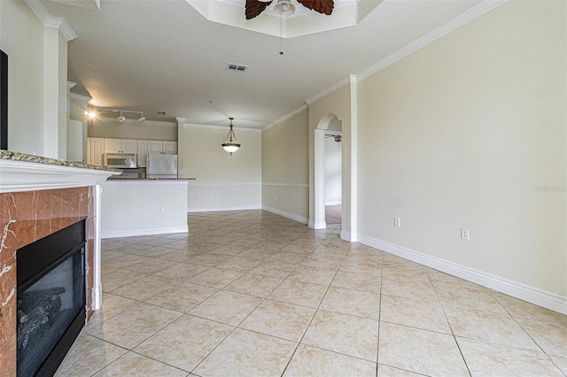 unfurnished living room featuring ceiling fan, light tile patterned floors, crown molding, and a tiled fireplace