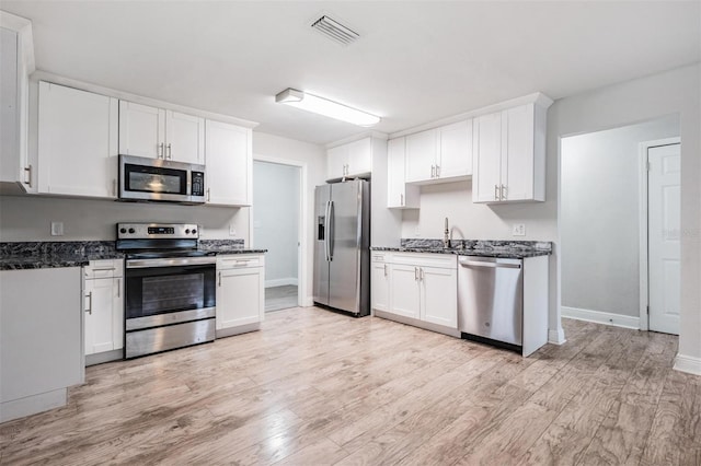 kitchen with white cabinetry, appliances with stainless steel finishes, light hardwood / wood-style flooring, and dark stone countertops