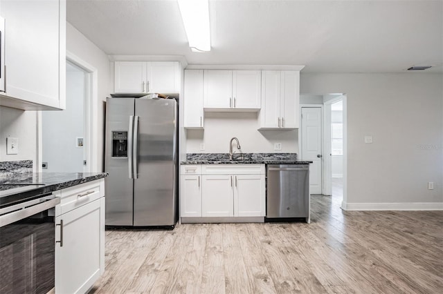 kitchen with stainless steel appliances, light hardwood / wood-style flooring, white cabinets, and dark stone counters