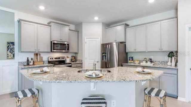 kitchen with a kitchen bar, light stone countertops, appliances with stainless steel finishes, sink, and a center island with sink