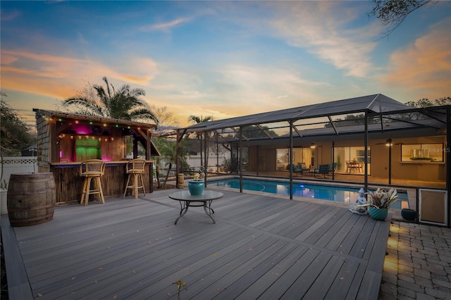 deck at dusk with a patio area, an outdoor bar, and glass enclosure