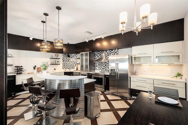 kitchen featuring white cabinets, appliances with stainless steel finishes, wall chimney exhaust hood, decorative light fixtures, and a kitchen breakfast bar