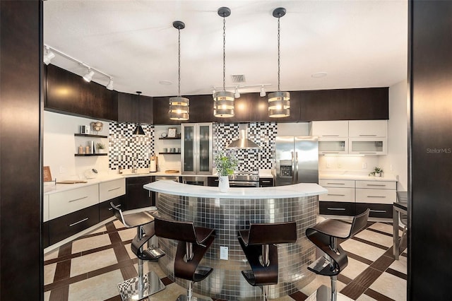 kitchen with appliances with stainless steel finishes, tasteful backsplash, white cabinetry, a breakfast bar, and wall chimney exhaust hood