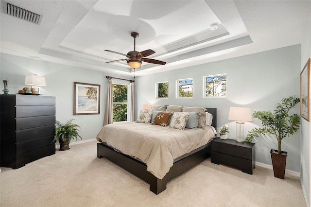 bedroom with light carpet, ceiling fan, and a raised ceiling