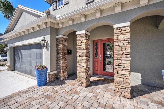 view of exterior entry with stone siding, driveway, and stucco siding