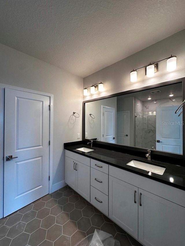 full bath with a textured ceiling, double vanity, a sink, and a shower stall