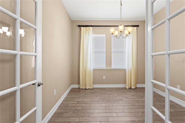 empty room with an inviting chandelier, light hardwood / wood-style floors, and french doors