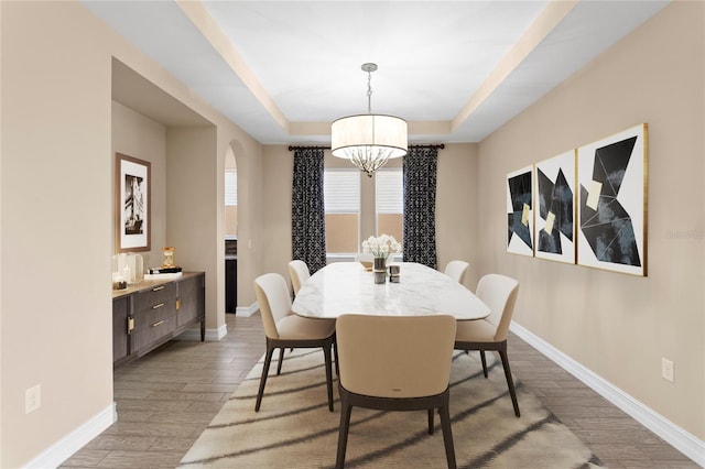 dining area with an inviting chandelier, light hardwood / wood-style floors, and a tray ceiling