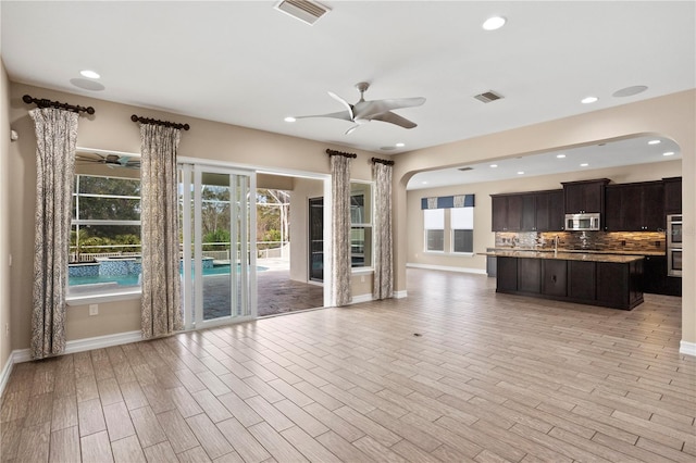 unfurnished living room with light wood-type flooring, a wealth of natural light, and ceiling fan