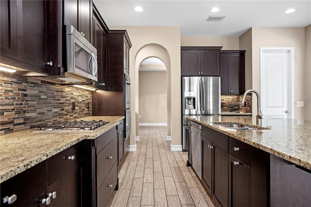 kitchen featuring sink, stainless steel appliances, dark brown cabinetry, light stone countertops, and light wood-type flooring