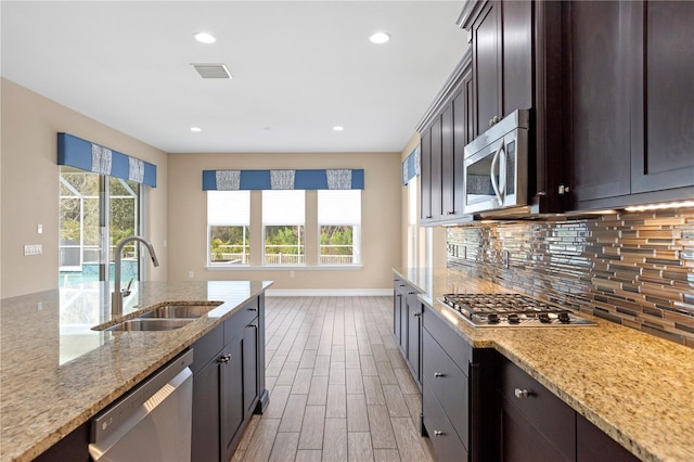 kitchen with tasteful backsplash, sink, light stone counters, stainless steel appliances, and dark brown cabinets