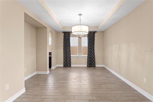 empty room with a notable chandelier, a tray ceiling, and light hardwood / wood-style flooring