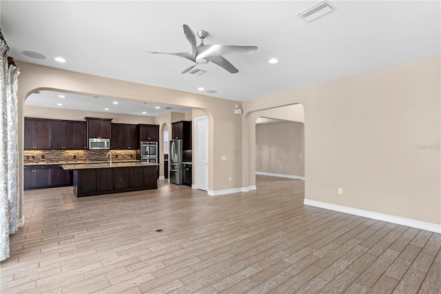 kitchen with dark brown cabinetry, a center island with sink, light hardwood / wood-style flooring, stainless steel appliances, and decorative backsplash