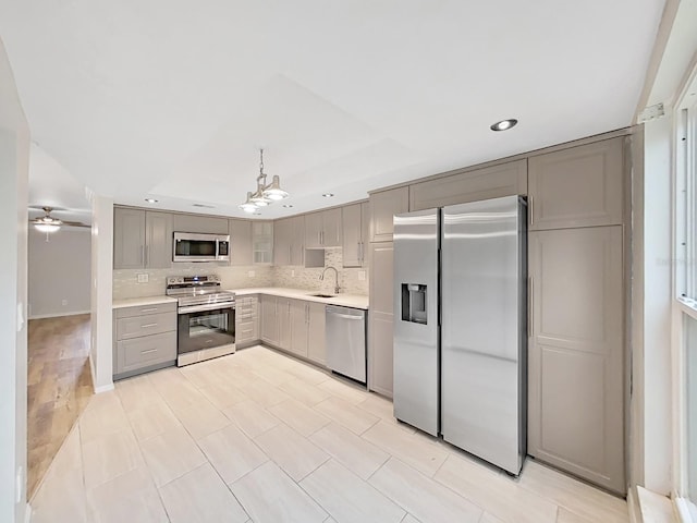 kitchen with ceiling fan with notable chandelier, stainless steel appliances, decorative backsplash, sink, and gray cabinetry