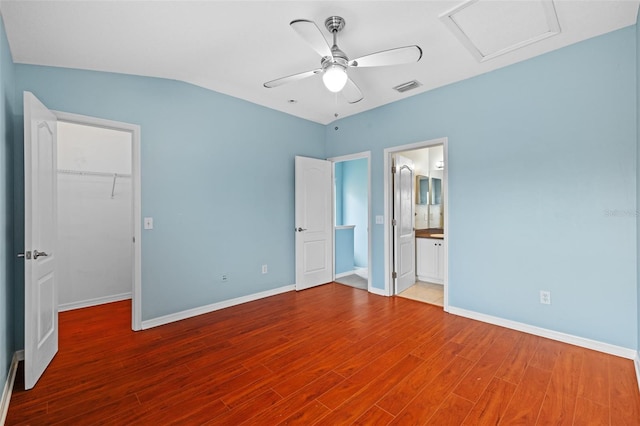 unfurnished bedroom with connected bathroom, wood-type flooring, a spacious closet, ceiling fan, and a closet