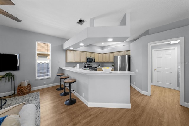 kitchen with a kitchen breakfast bar, stainless steel appliances, light hardwood / wood-style floors, light brown cabinetry, and kitchen peninsula