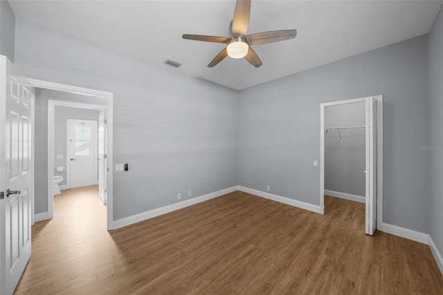 unfurnished bedroom featuring ceiling fan, a walk in closet, hardwood / wood-style floors, and a closet