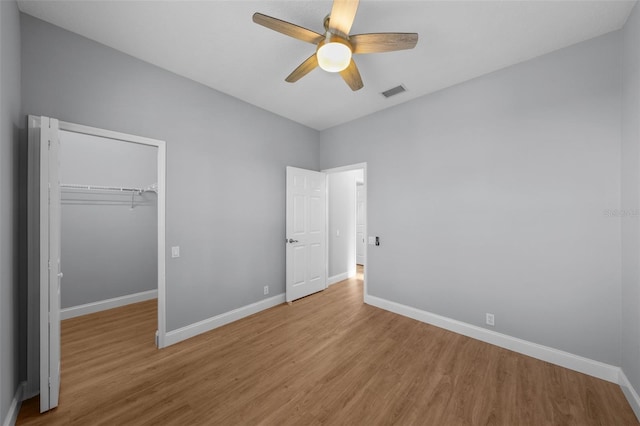 unfurnished bedroom with ceiling fan, a walk in closet, a closet, and light wood-type flooring