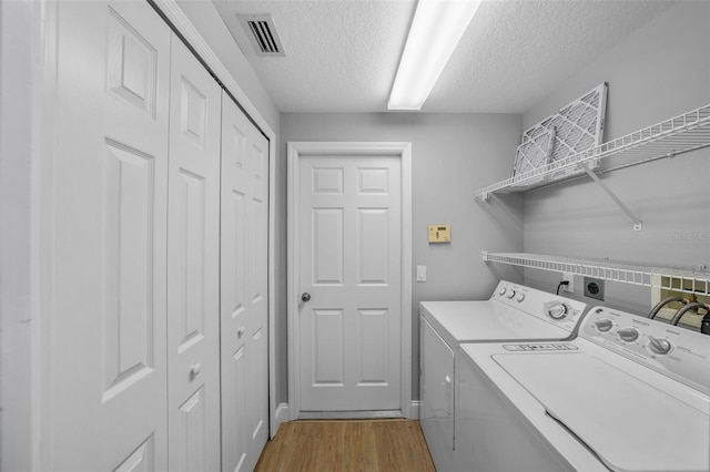 laundry room featuring light hardwood / wood-style flooring, washer and clothes dryer, and a textured ceiling