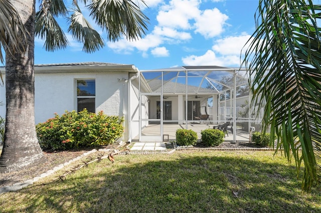 rear view of property featuring ceiling fan, a patio, glass enclosure, and a lawn