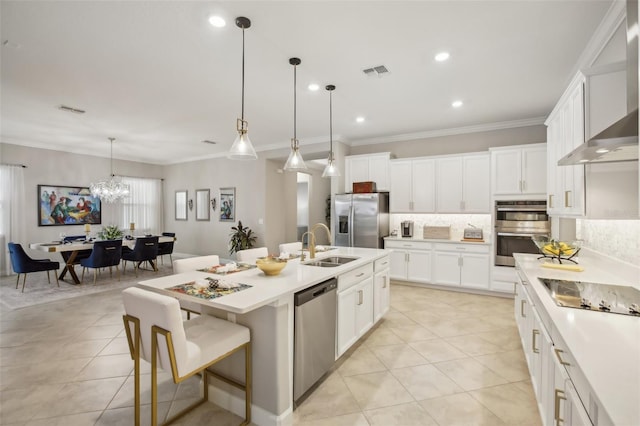 kitchen featuring an island with sink, sink, hanging light fixtures, stainless steel appliances, and wall chimney range hood