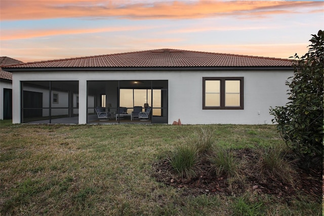 back house at dusk featuring a patio and a lawn