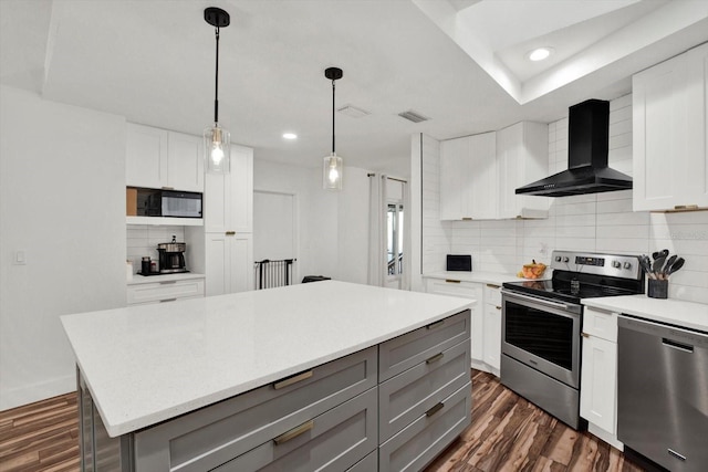 kitchen with dark hardwood / wood-style floors, white cabinets, a center island, stainless steel appliances, and wall chimney exhaust hood