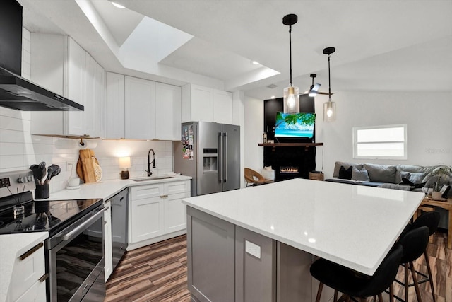 kitchen featuring wall chimney exhaust hood, sink, a kitchen island, stainless steel appliances, and white cabinets