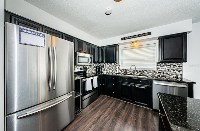 kitchen with dark wood-type flooring, sink, dark stone counters, stainless steel appliances, and decorative backsplash