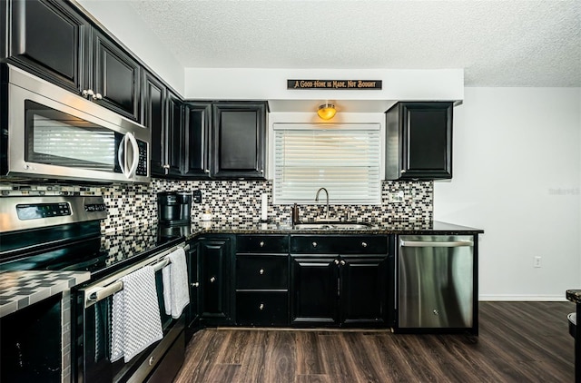 kitchen featuring sink, dark wood-type flooring, appliances with stainless steel finishes, dark stone countertops, and a textured ceiling