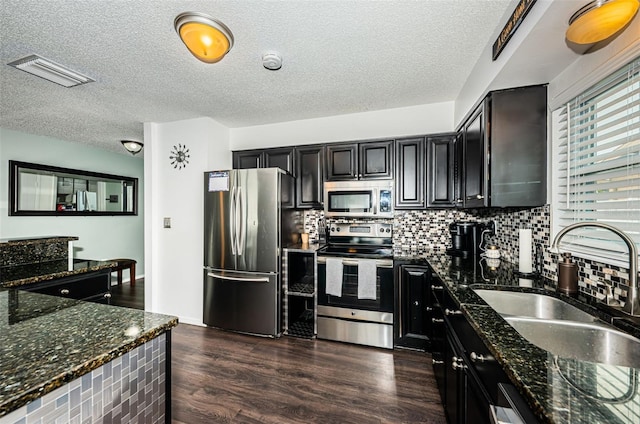 kitchen with sink, dark stone countertops, appliances with stainless steel finishes, dark hardwood / wood-style flooring, and decorative backsplash